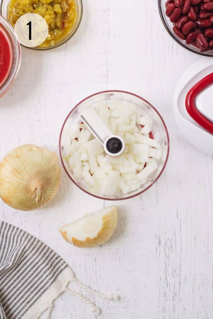 Handheld food chopper with chopped onions inside and to left with black and white linen in lower left and bowls of additional ingredients to make Taco Quinoa. 