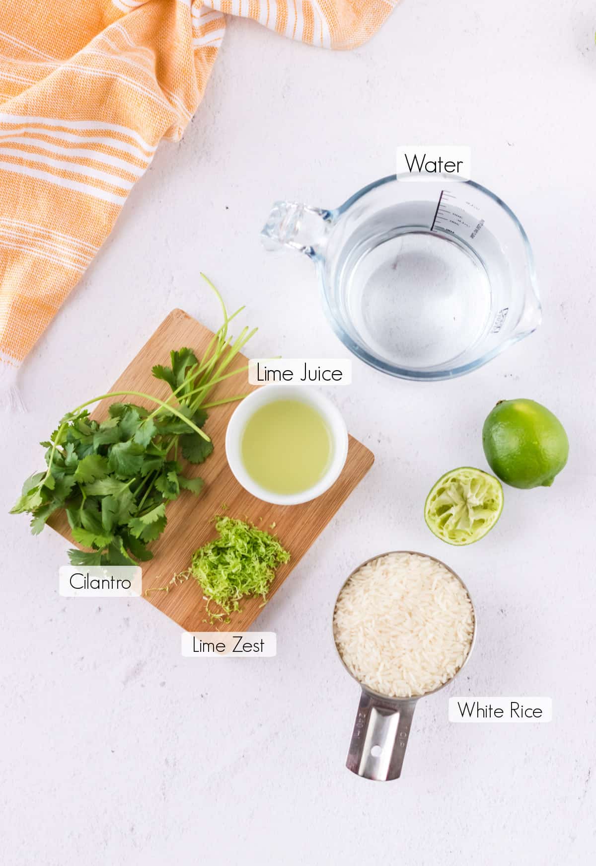 Labeled ingredients to make cilantro lime rice with orange linen in upper background.