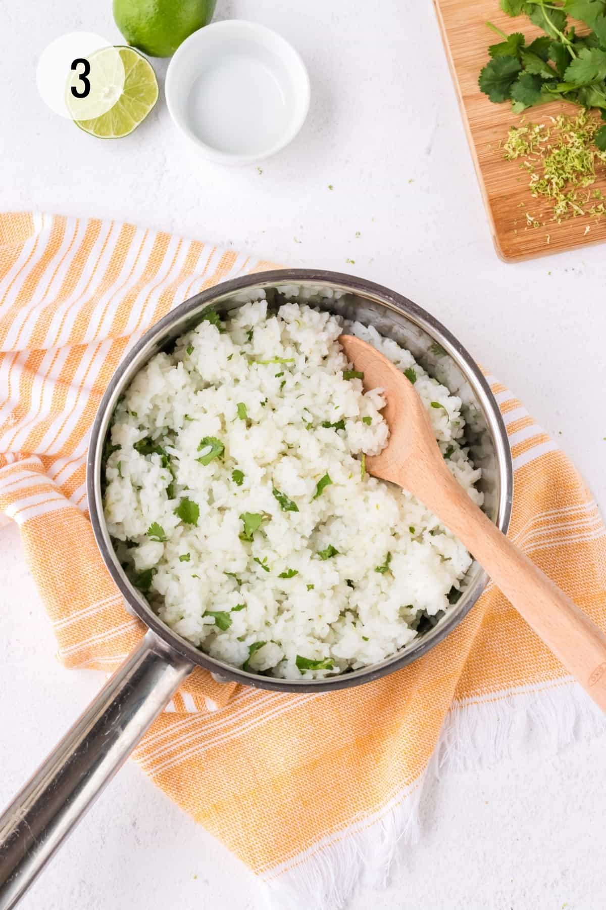 Metal saucepan with white rice and chopped cilantro with wooden spoon and orange linen and limes, zest and cilantro sprigs in upper background. 