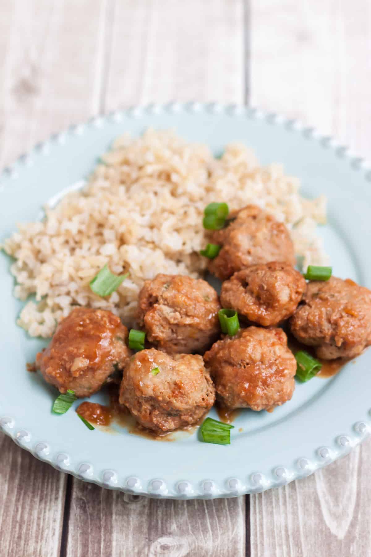 Ground turkey meatballs with peach ginger sauce and brown rice garnished with green onions all on a blue plate.