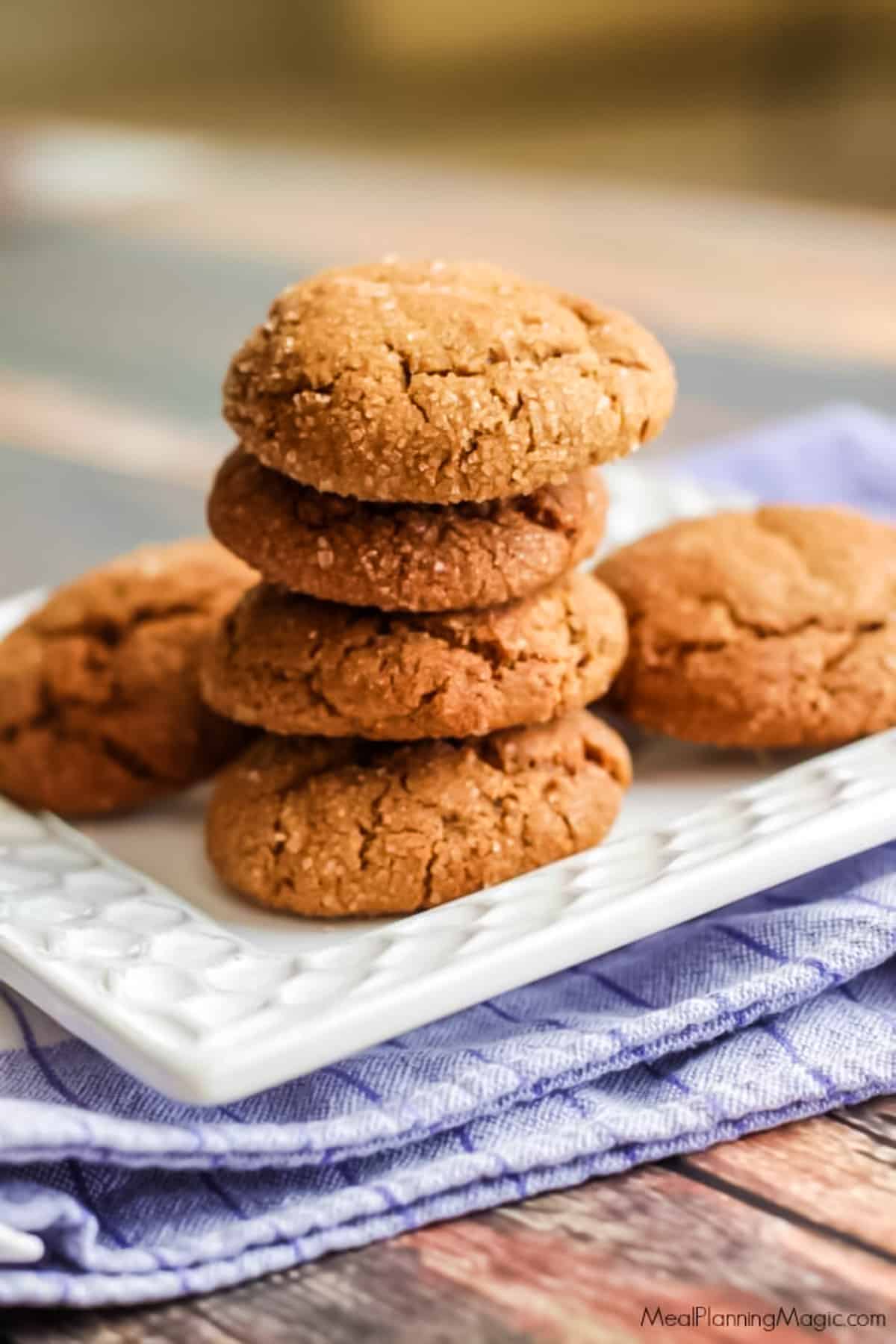 Bite-sized Chewy Ginger Molasses Cookies stacked on a white plate on a blue and white napkin.