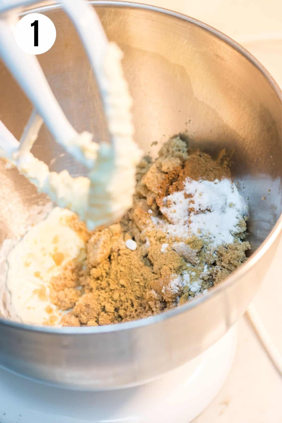 Metal mixing bowl with butter, brown sugar, cinnamon and baking soda being mixed by stand mixer paddle. 