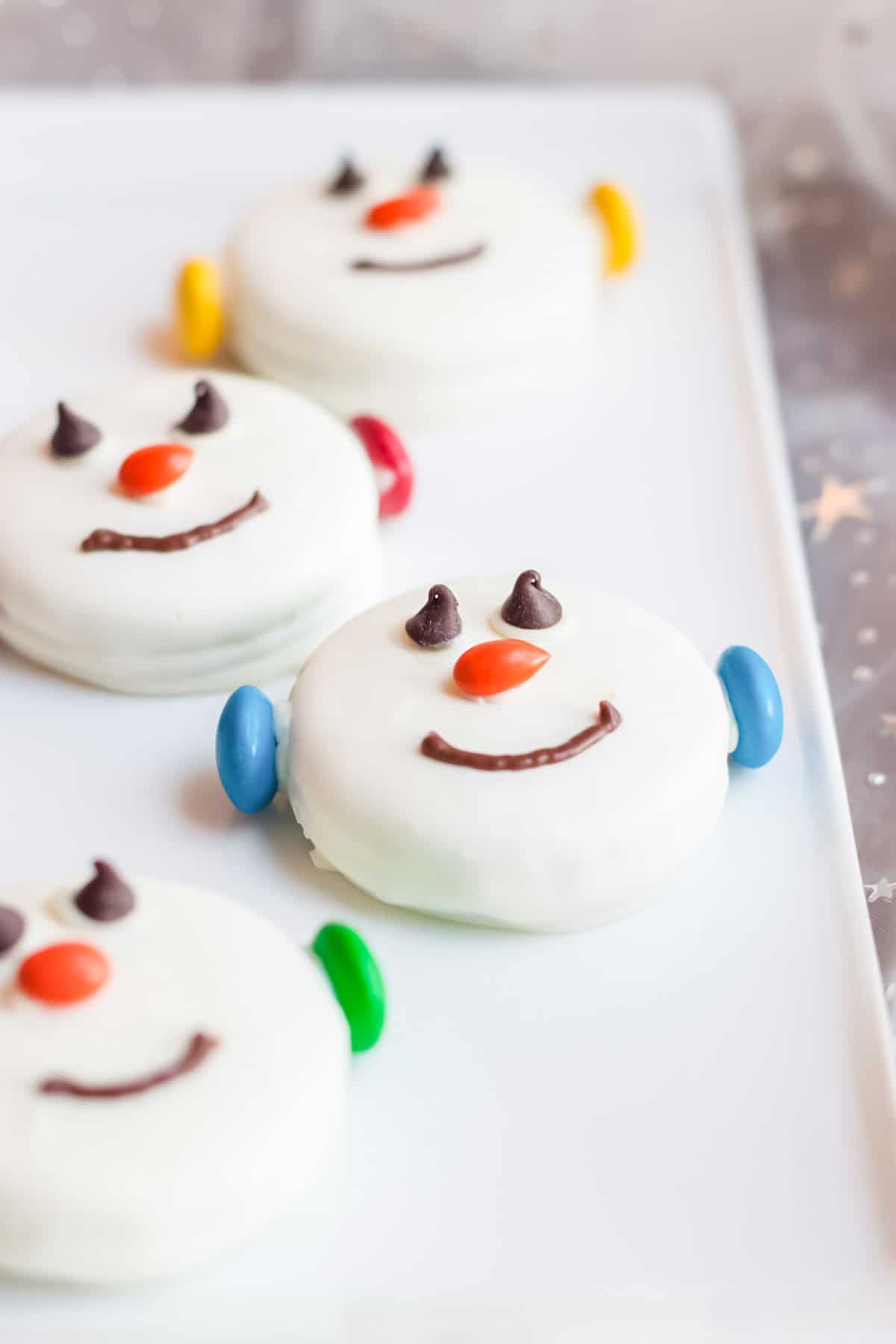 Platter of white chocolate fudge covered Oreos decorated with candies to look like snowman faces.