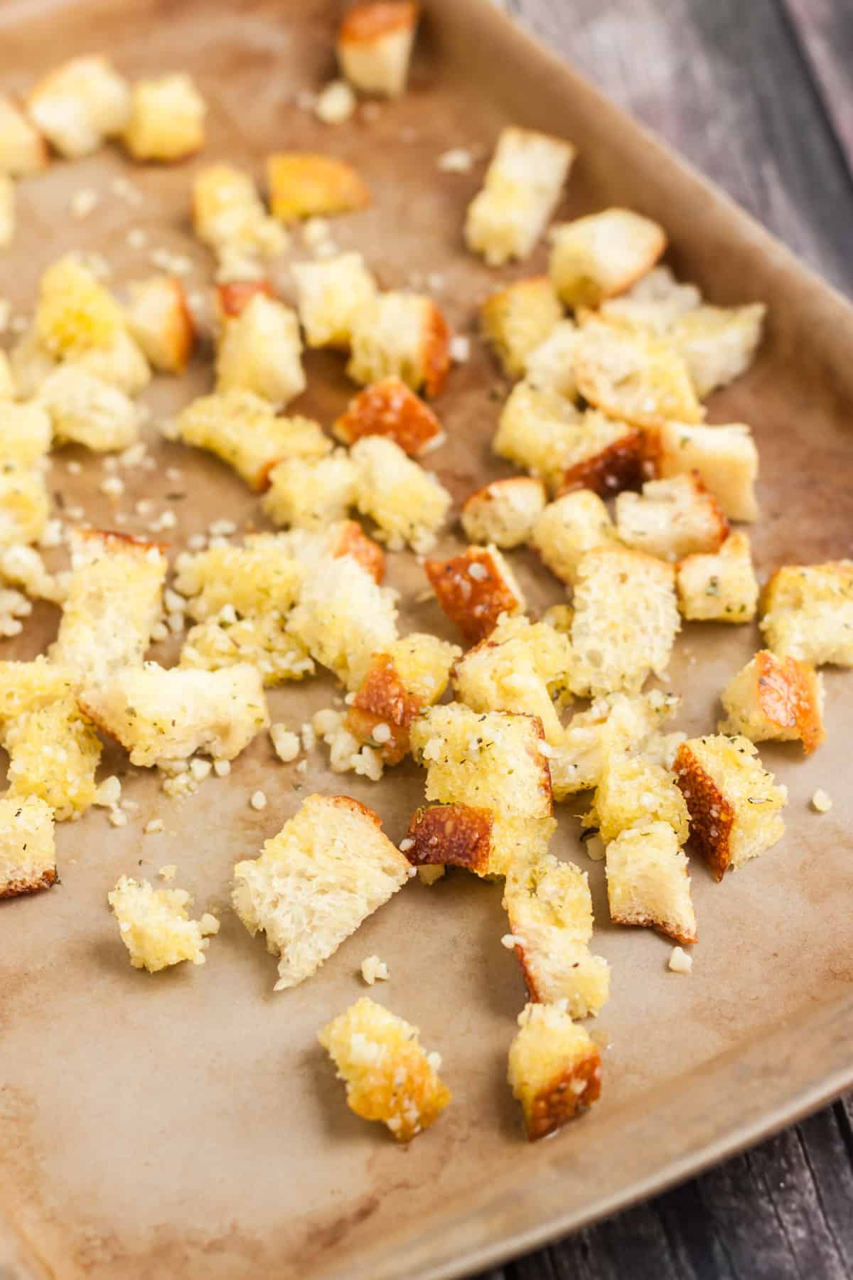 stone baking sheet with cubes of bread croutons sprinkled with parmesan cheese and herbs